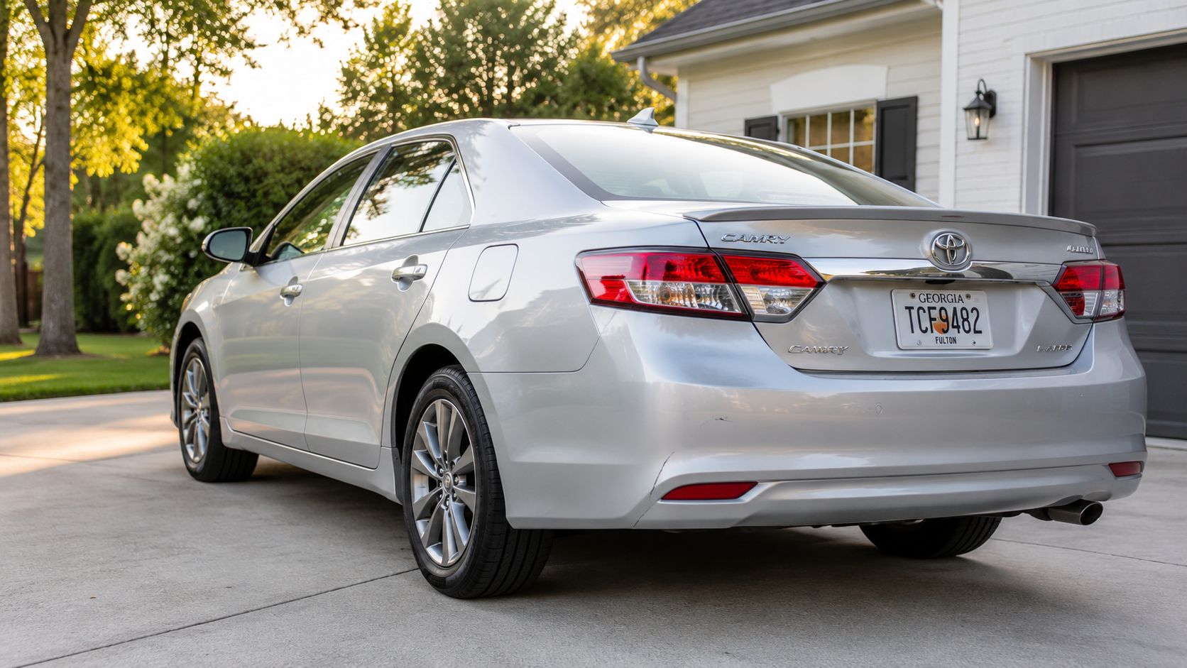 A silver Toyota Camry sedan parked in a suburban residential driveway during a sunny golden hour.